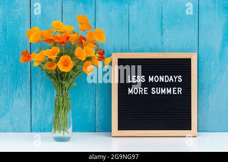 Less mondays more summer. Motivational quote on letter board and bouquet orange flowers on white table against blue wooden wall. Concept inspirational Stock Photo