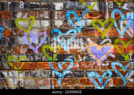 Painted love: Colourful hearts spray painted on a distressed red brick wall in Birmingham, England, UK. Stock Photo