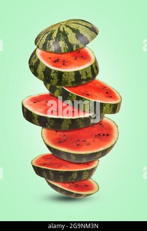Ripe watermelon cut into pieces flying in the air on a light green background. Minimal composition with floating, flying, levitating sliced fresh wate Stock Photo