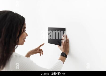 African american woman using digital tablet with blank black screen with smart home control system app, mockup Stock Photo