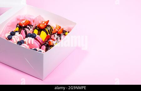 Macaroons with blueberry and strawberry in paper box. Colourful and Delicious dessert with chocolate. Close up, top view Stock Photo