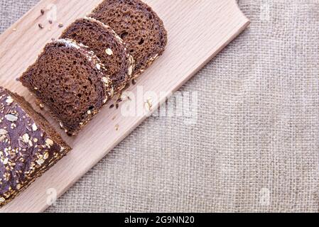 Dark rye sliced bread with whole sunflower seeds, flaxseeds and oatmeal on top on a board, copy space. Stock Photo