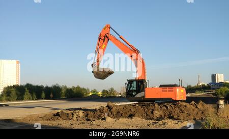 Yellow excavator machine during excavation work on construction site. Process of building new road or urban highway Stock Photo