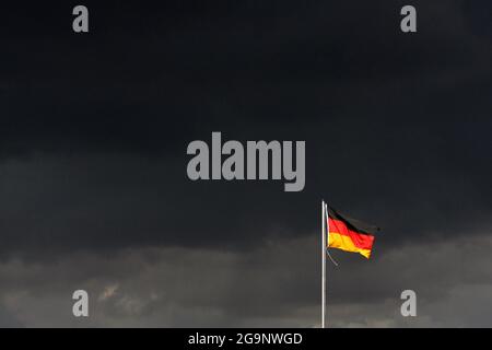 Schleibnitz, Germany. 27th July, 2021. Dark rain clouds are gathering over a waving German flag. Apart from isolated showers it should remain dry in the coming days. It's getting cooler towards the end of the week. Credit: Klaus-Dietmar Gabbert/dpa-Zentralbild/ZB/dpa/Alamy Live News Stock Photo