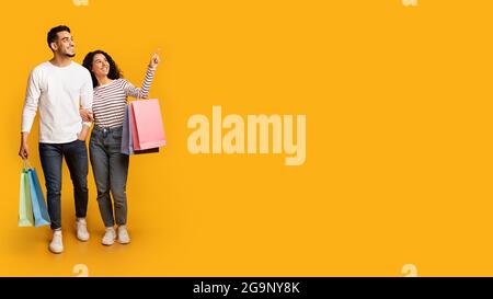 Seasonal Discounts. Smiling Arab Spouses Walking With Shopping Bags And Pointing Aside Stock Photo