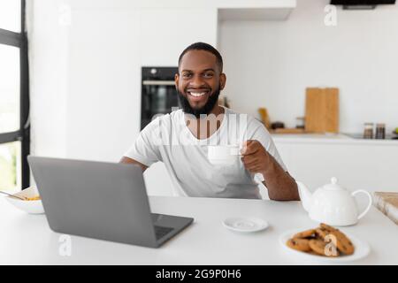 African American man using laptop drinking coffee looking at camera Stock Photo