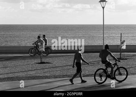 Salvador, Bahia, Brazil - December 16, 2018: People ride bicycles along the Rio Vermelho beachfront in Salvador. A day with strong sunshine that attra Stock Photo
