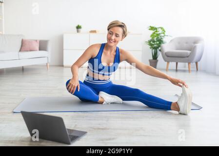 Cheerful woman stretching leg muscles using pc Stock Photo