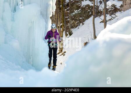 Woman ice climber tying a rope to his harness, preparing for a climb Stock Photo