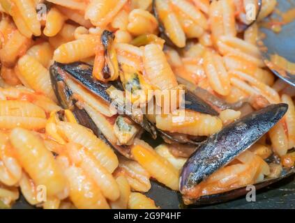 Close-up of a typical Italian dish. Sardinian gnocchi with black mussels with tomato, onion, garlic and pepper. Stock Photo