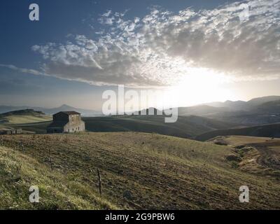 the sun is setting on the countryside with abandoned farmhouse in the sicilian hinterland