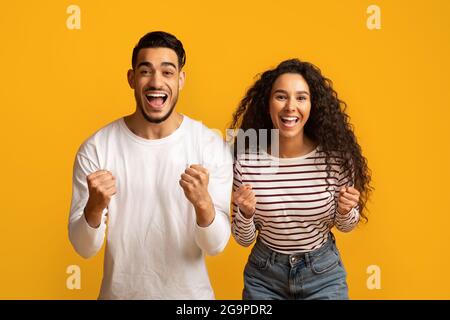 Hooray. Euphoric Middle Eastern Couple Raising Fists And Exclaiming With Excitement Stock Photo