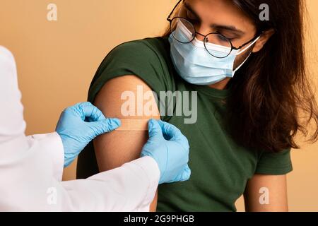 Nurse in workwear making vaccination for middle-eastern guy Stock Photo