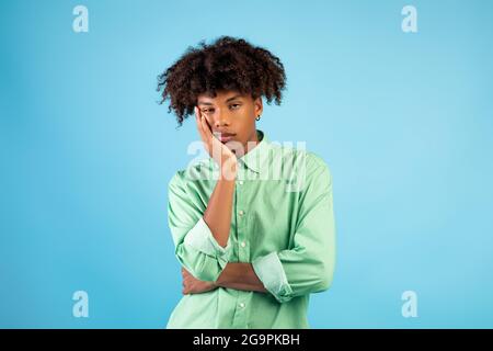 Portrait of black teen guy feeling bored, leaning on his hand, having dull day on blue studio background Stock Photo