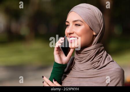 Happy Islamic Woman In Hijab Talking On Mobile Phone Outside Stock Photo