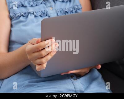 A woman watching a video on a laptop while sitting on a couch. Close up. Stock Photo