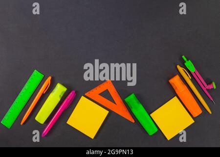 Back to school. Green, yellow, pink, orange office supplies are on the black board, the table. Top view. Rulers, markers, felt tip pens, compasses, pe Stock Photo