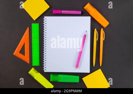 Back to school. On black table lies notebook checkered with pencil for text with empty space. All around are green, yellow, pink, orange stationery. R Stock Photo