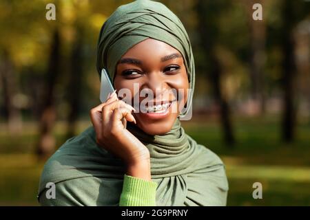 Cheerful African American Muslim Female Talking On Cellphone Standing Outdoors Stock Photo