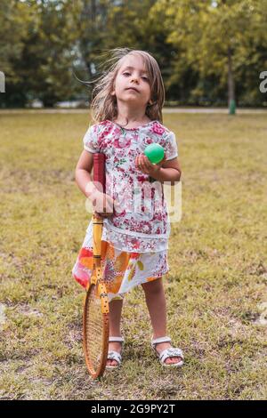 portrait of smiling cute little girl playing with an old tennis racket in a public park Stock Photo