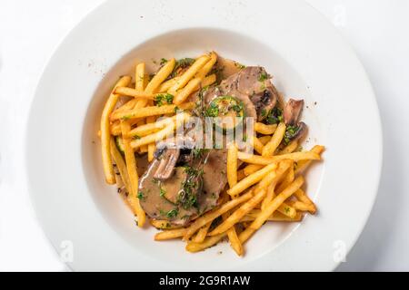 Roast pork on toast with mushrooms and sauce, served with french fries in white plate. Close-up top view Stock Photo