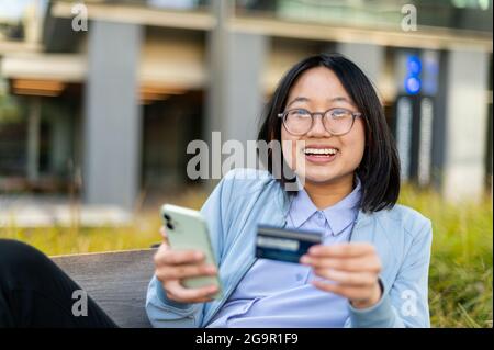 Young woman looking at camera holding credit card and cell phone Stock Photo