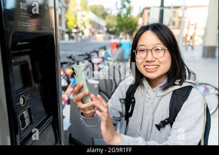 Young woman using smart phone at urban bike rental station Stock Photo