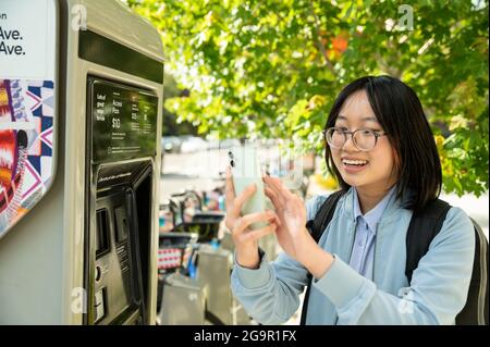 Young woman using cell phone at bike share station while commuting Stock Photo