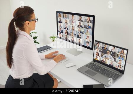 Woman using desktop and laptop computers for online meeting with diverse business team Stock Photo