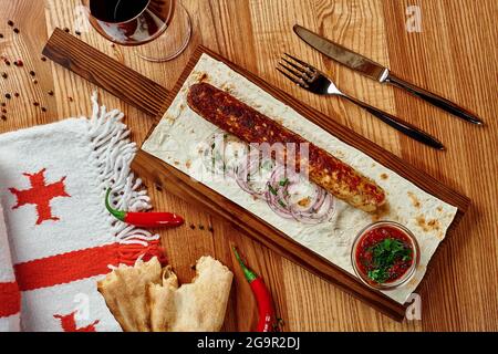 Chicken lula kebab on wooden table with lavash, onions, greens and satsebeli Stock Photo