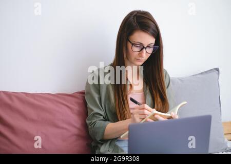 Concentrated young woman freelancer making notes. work from home. Slow life concept. Stock Photo