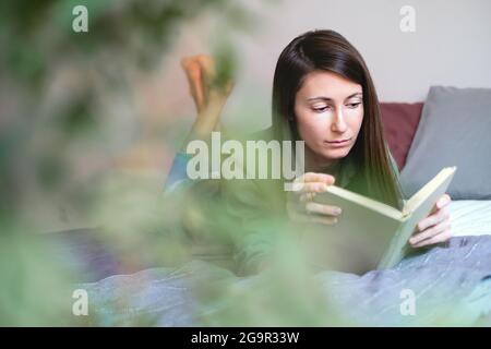 Young woman lying in bed and reading book. Domestic life. Slow life concept. Home hobbies. Stock Photo