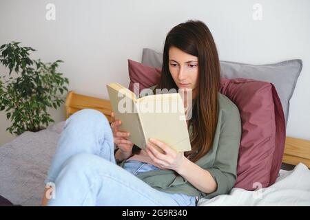 Young woman lying in bed and reading book. Domestic life. Slow life concept. Home hobbies. Stock Photo