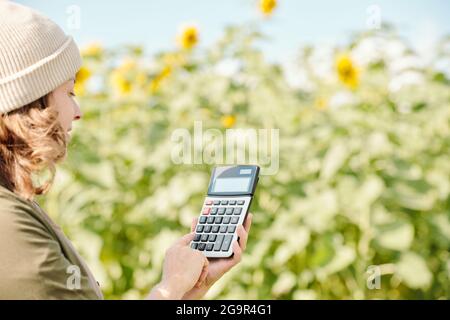 Hands of senior male farmer holding calculator with one on its display and pushing button with this number against green plants and leaves Stock Photo