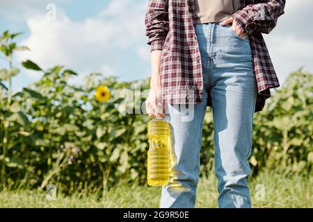 Mature cheerful female farmer in beanie and workwear looking at you with smile while standing in front of camera against green field and sky Stock Photo