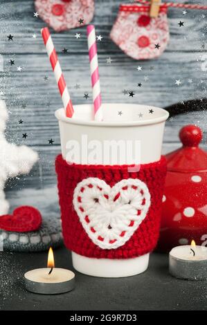 Cup with straws in red knitted warmer on blue wooden background.Christmass set with teapot and lit candles Stock Photo