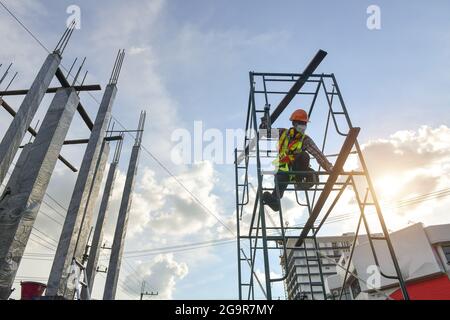 Construction worker wearing safety work at high uniform on scaffolding at construction site on during sunset, selective focus Stock Photo