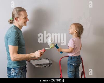 Person holding paint roller over gray wall. Father with child doing decoration and re-design of room, having fun during apartment renovation Stock Photo