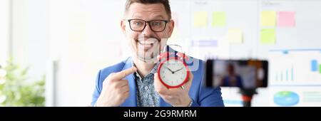 Portrait of smiling businessman holding red alarm clock in his hand Stock Photo