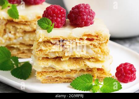 Pieces of Napoleon cake decorated with raspberries and lemon balm leaves on a light background. Stock Photo