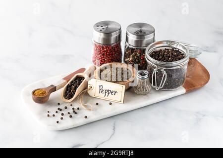 An arrangement of different types of pepper in various containers on a marble slab. Stock Photo