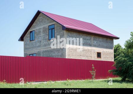 Private house under construction with windows and a roof behind a fence. Country housing. Stock Photo