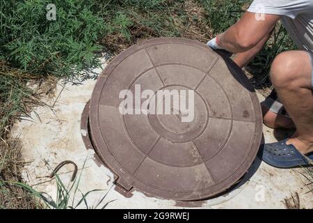 The man opens the manhole cover of the water well. Checking and fixing water metering. Stock Photo