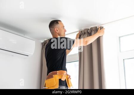 worker repairman hanging and fixing the curtain on the window Stock Photo