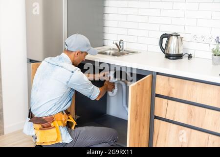 plumber fixes sink siphon by two pipe-wrenches in kitchen. Stock Photo