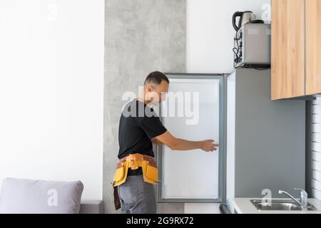 Young Male Technician Checking Fridge With Digital Multimeter Stock Photo