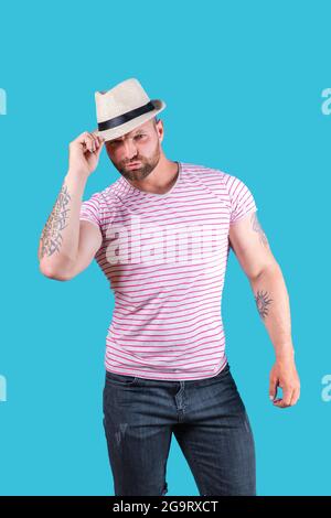Fashionable muscular bearded man in straw hat posing in studio over blue background Stock Photo