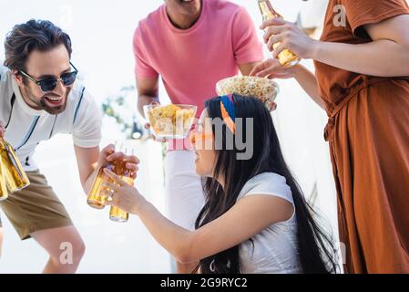 happy man in sunglasses giving beer to asian woman near blurred interracial friends Stock Photo