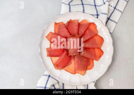 Beef jerky pieces. Dried beef meat on white plate, top view, flat lay with copy space Stock Photo