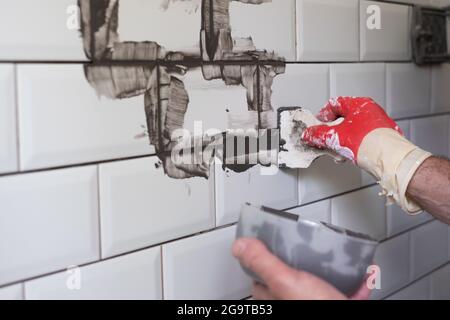 Worker applies grey grout at white tiles with rubber trowel. Stock Photo